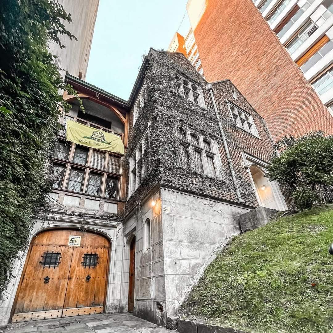 Fachada de La Crypta en Belgrano: casona de piedra con hiedra y portón de madera